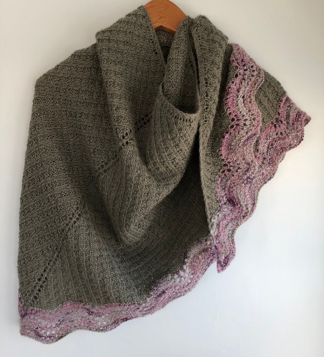 Green knit shawl with multicolored pink border on hanger