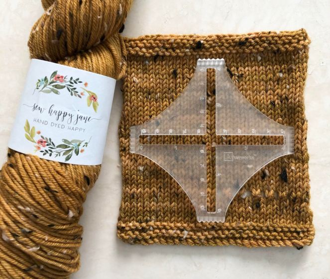 skein of golden tweed yarn and swatch with stitch counter