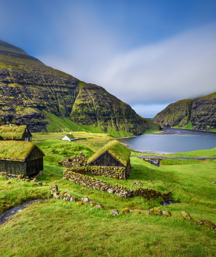 green grass, small stone houses, mountains, blue sky with white clouds