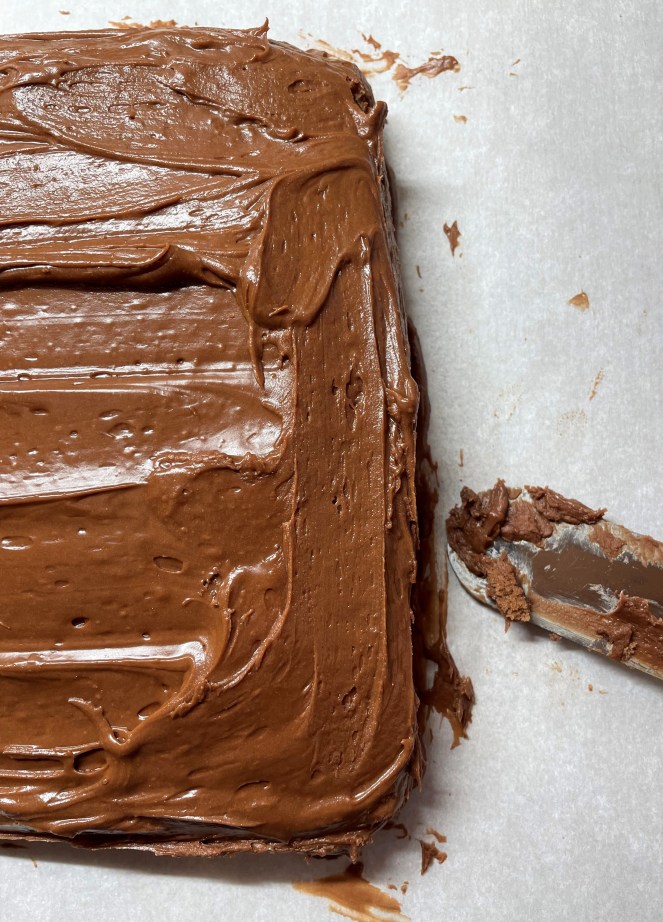 portion of a square chocolate cake and spatula with frosting
