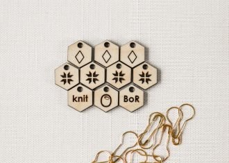 ten laser cut knitting stitchmarkers and gold coil-less safety pins on linen background