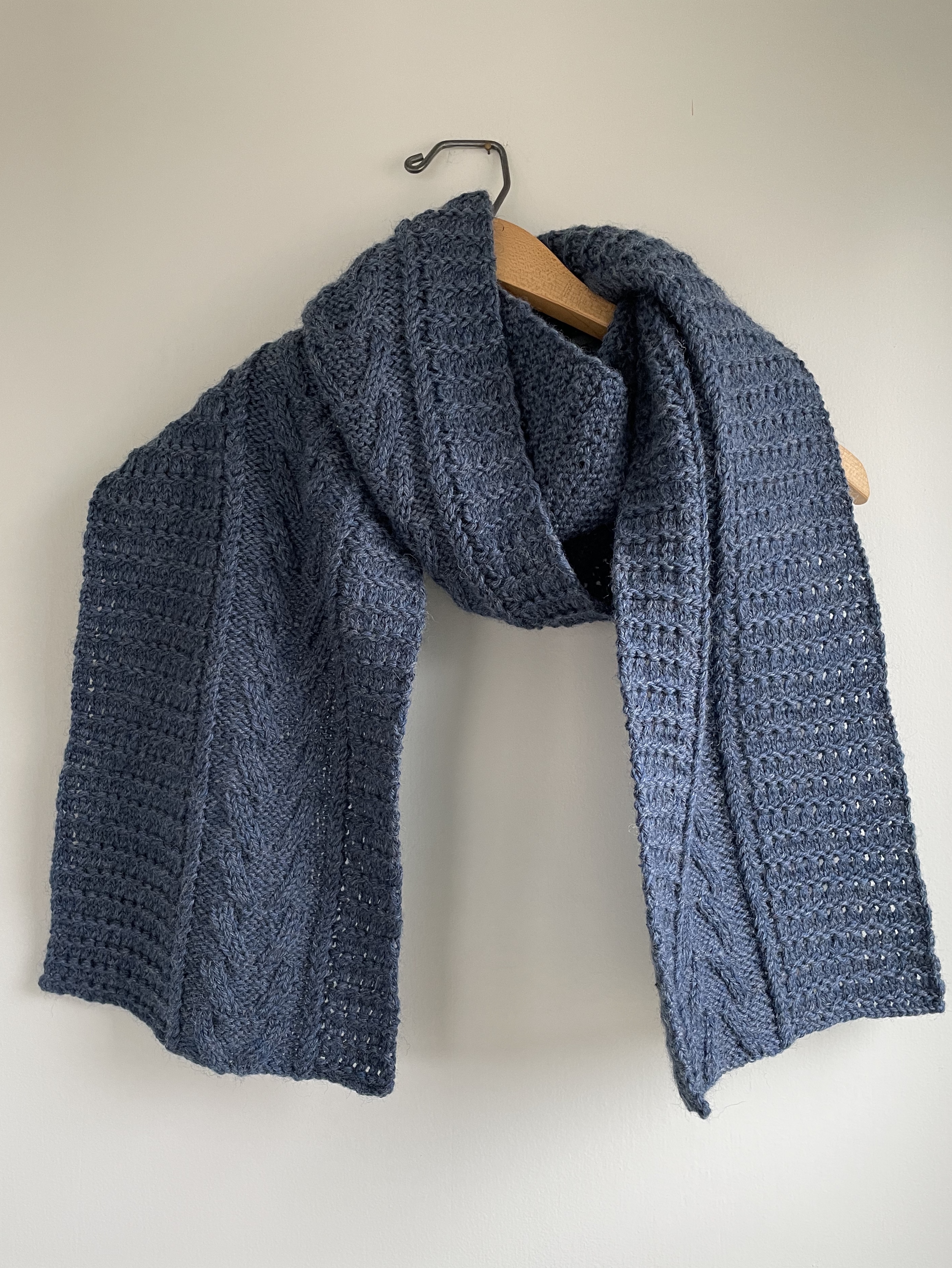 handknit scarf with cable stitches using blue yarn on a wooden hanger