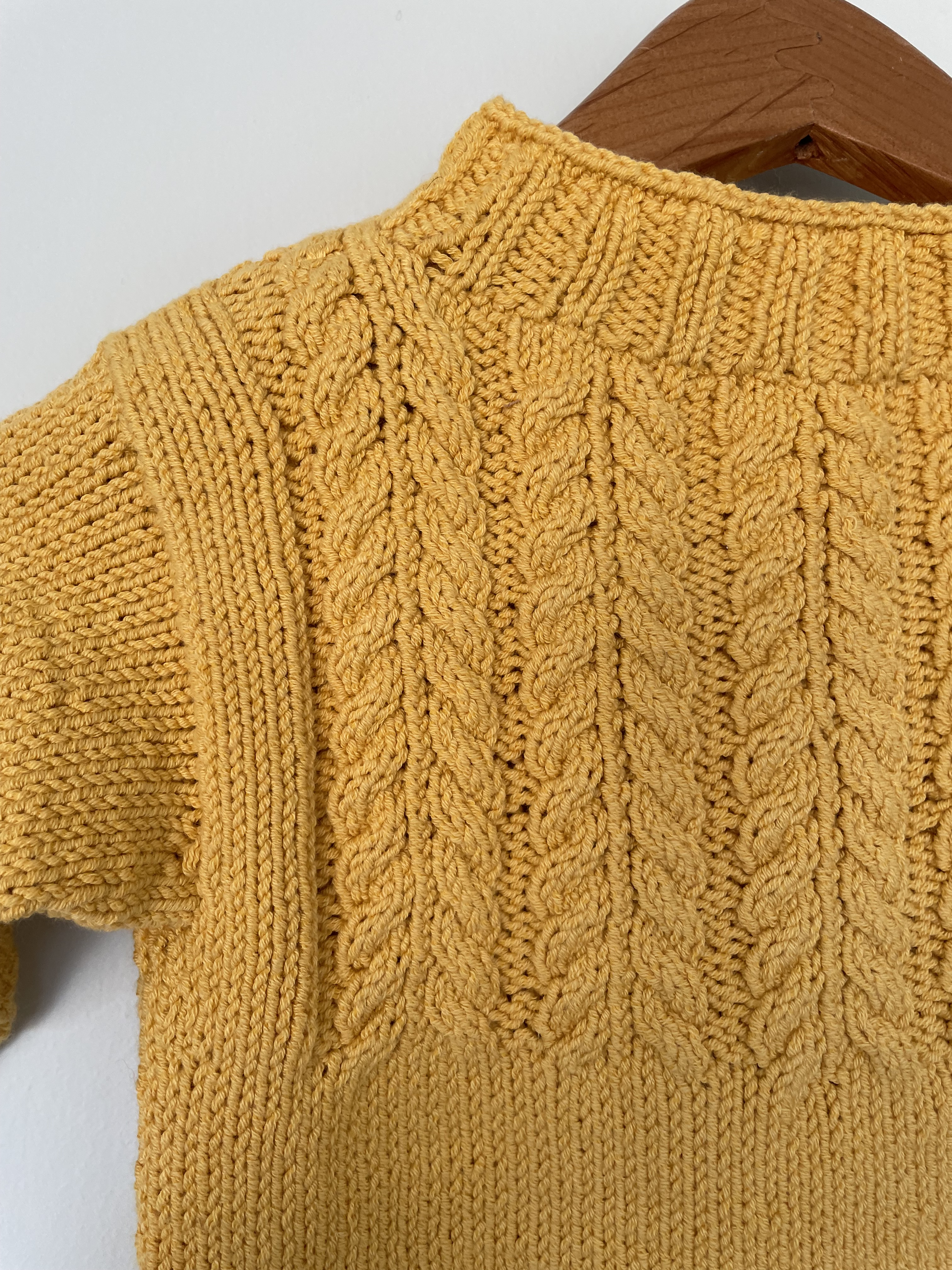 yellow sweater with cable stitched yoke on wooden hanger