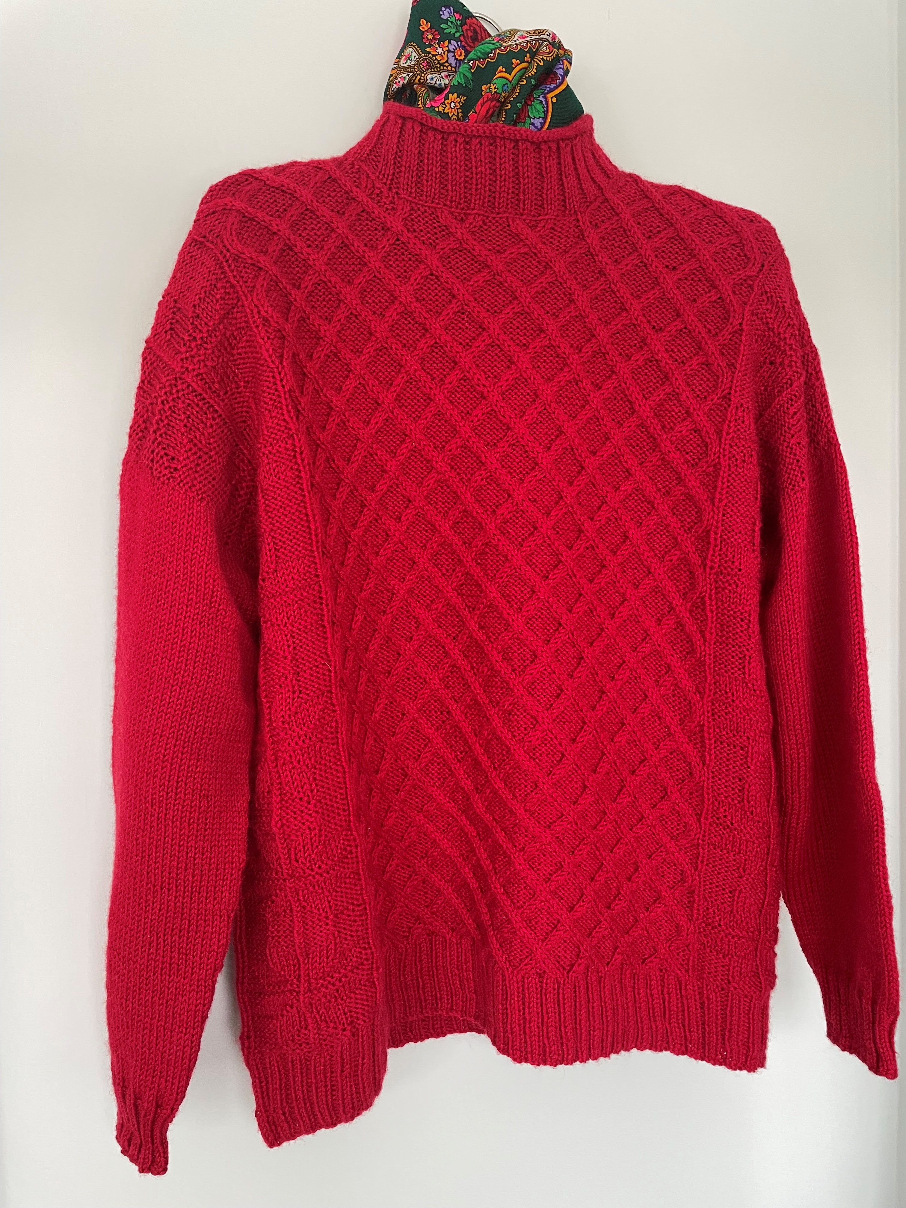 red hand knit sweater with cables on front and green scarf at the neck