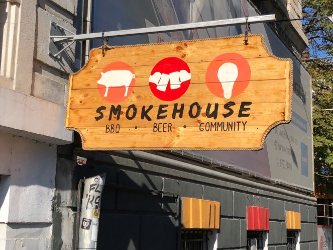 wooden smokehouse sign hanging on a gray stone building