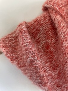 handknit coral colored cowl on wooden hanger