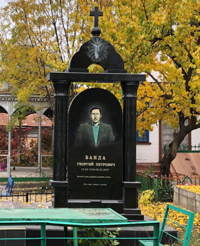 green table and chair in foreground with black gravestone with Cyrillic writing