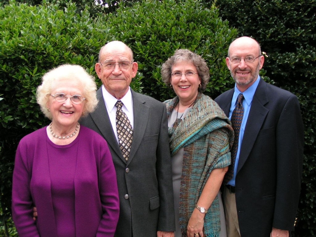 two women and two men dressed for a party and standing against green shrubbery