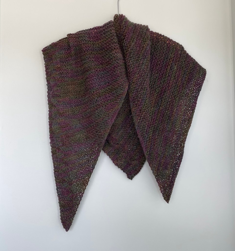hand knit triangular green and purple shawl draped on wooden hanger