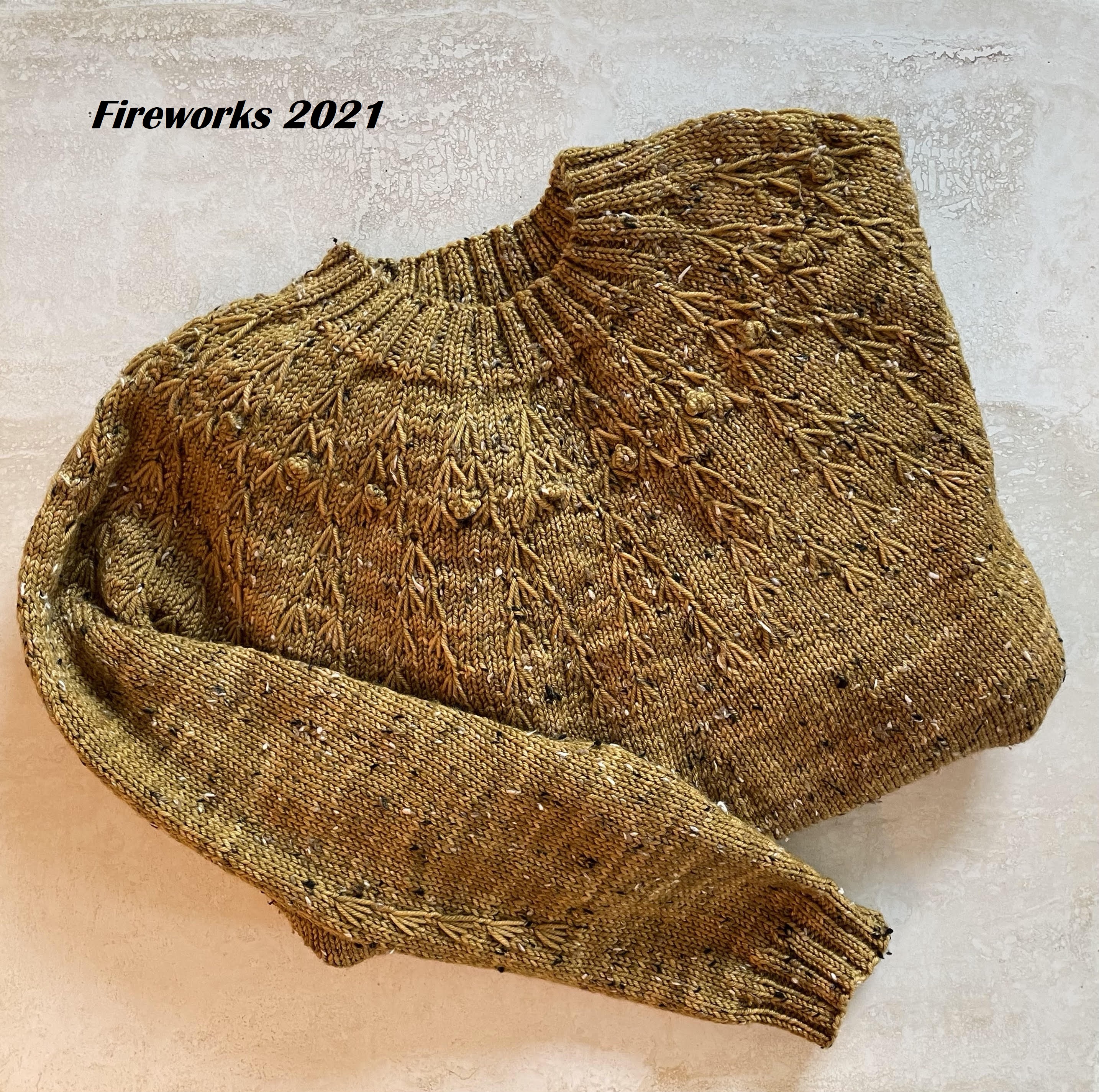 handknit gold sweater folded on marble background with note that reads Fireworks 2021