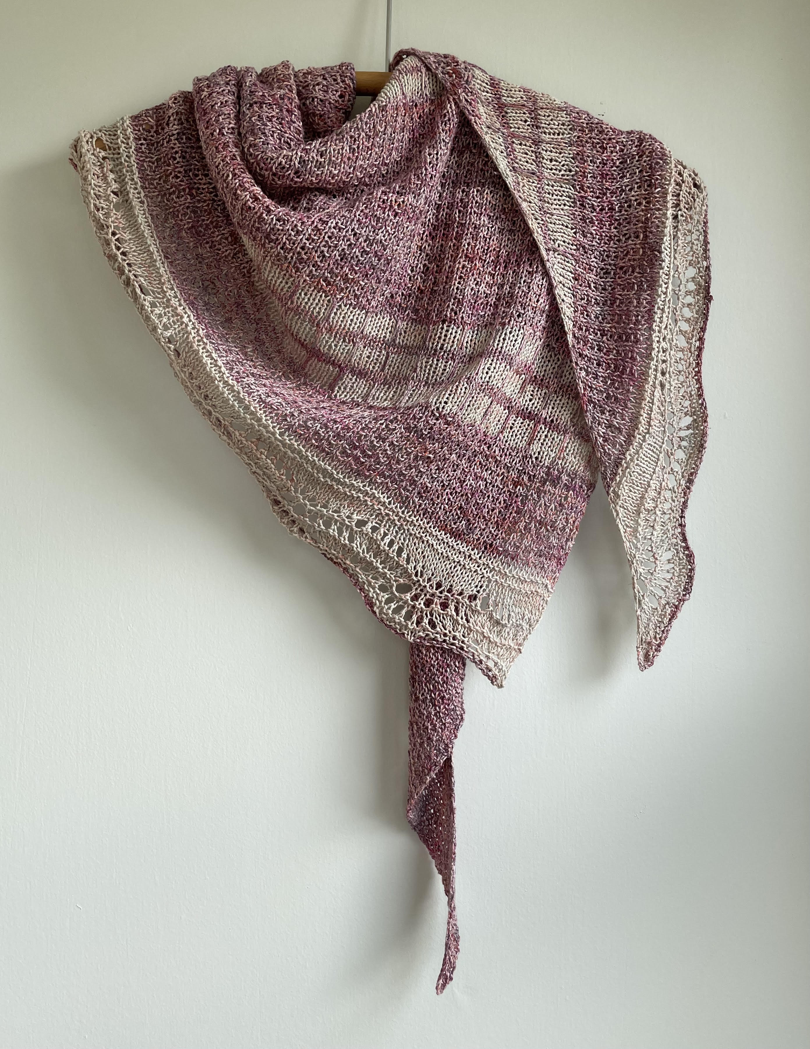 pink and cream handknit triangular shawl draped on a wooden hanger