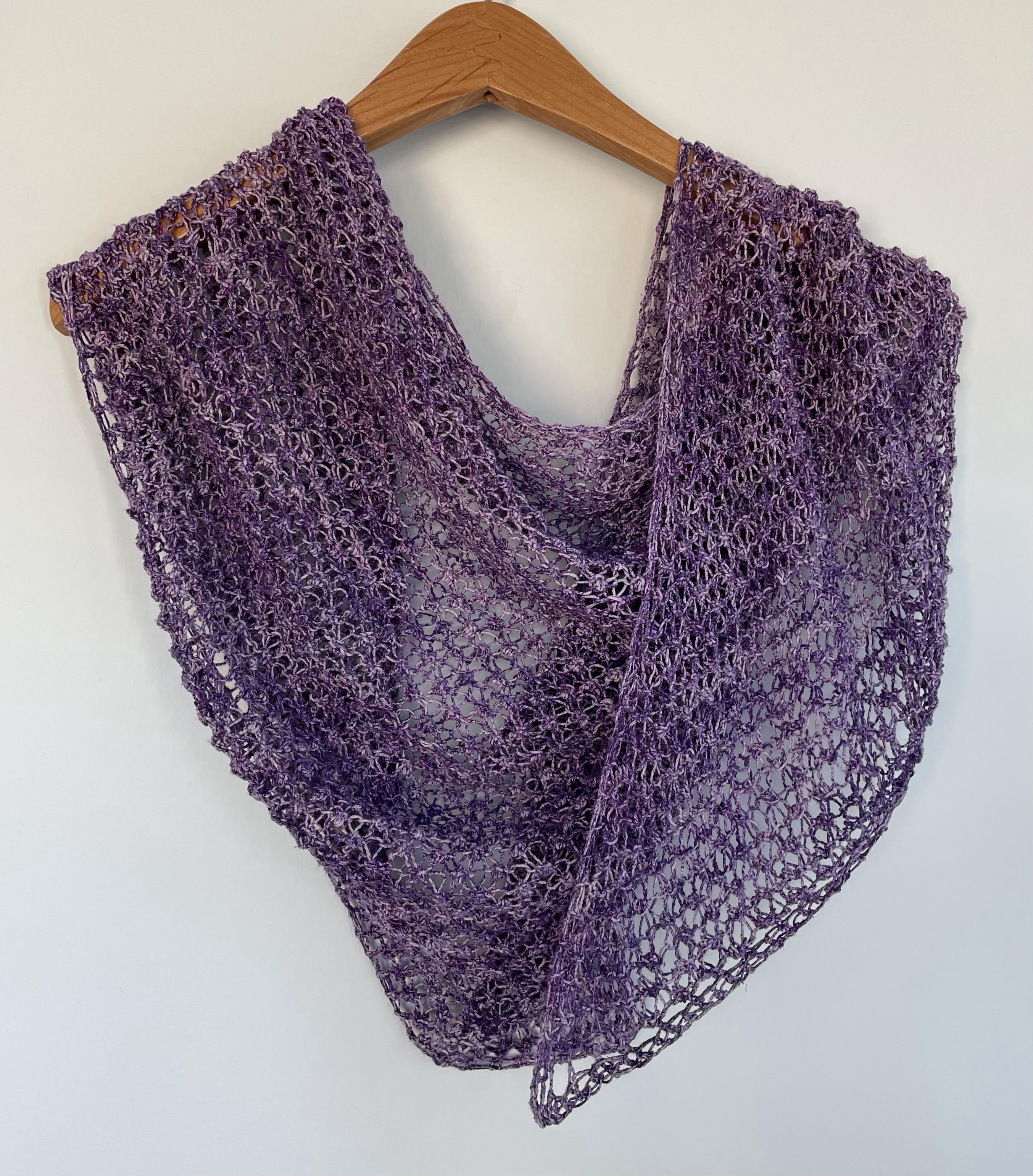 vibrant violet handknit lace shawl draped on a wooden hanger