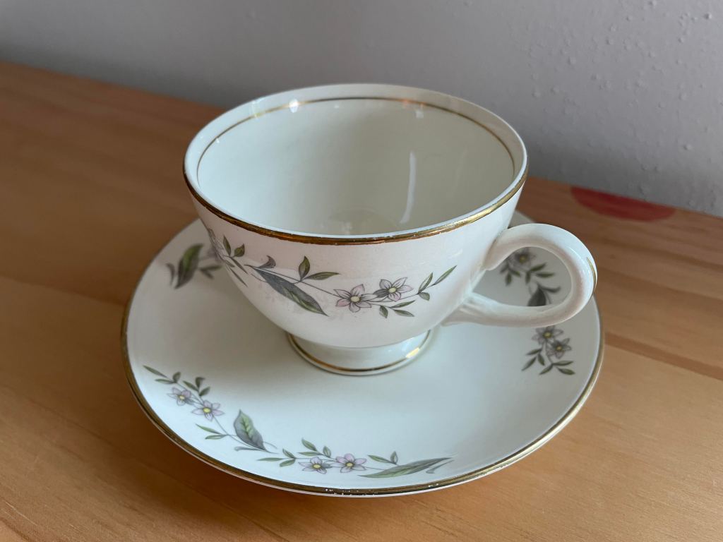 white china cup and saucer with small pick flowers decorating the border and edged with gold