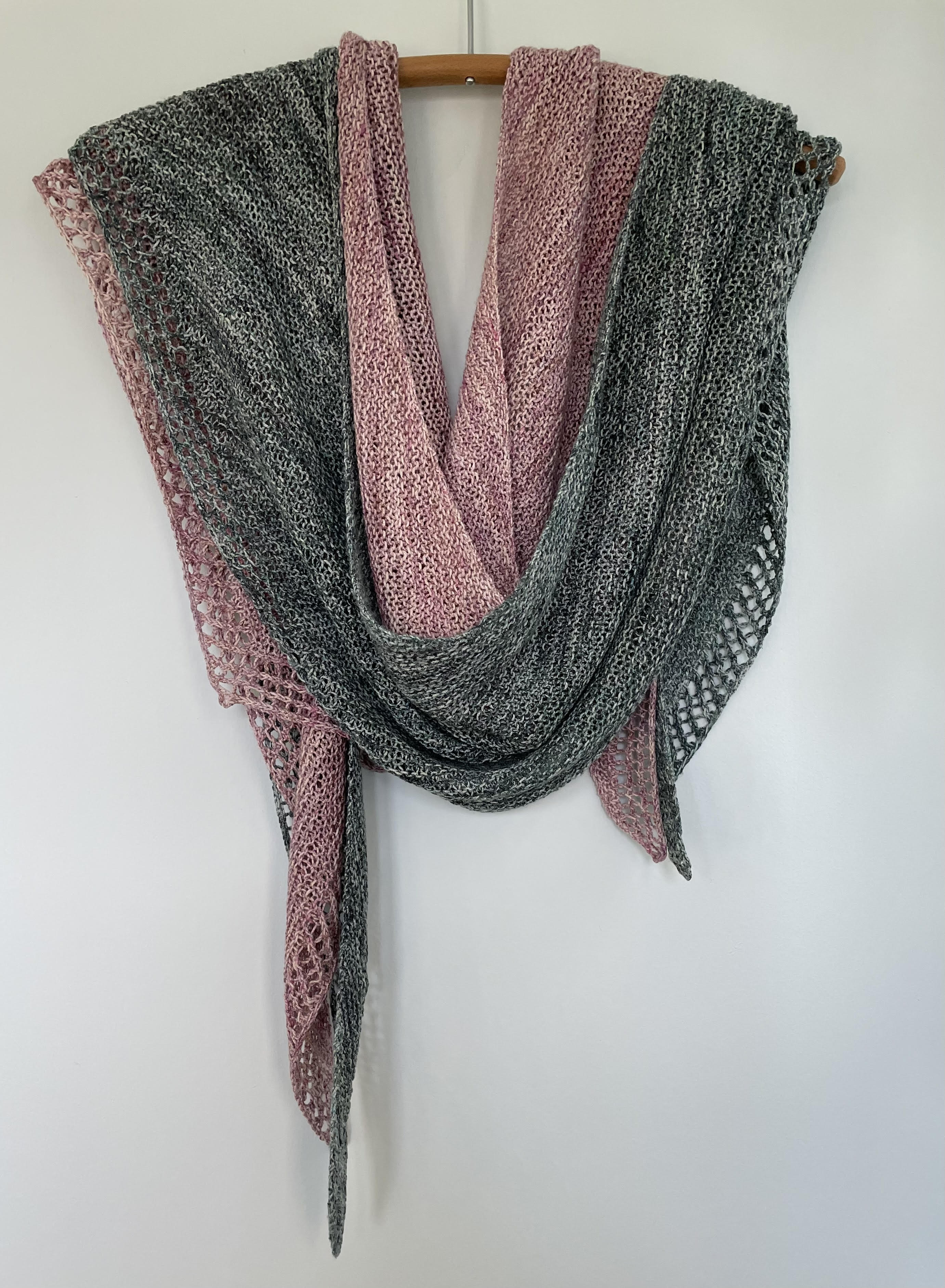 two handknit silk shawls, one pink and one green, draped on a wooden hanger