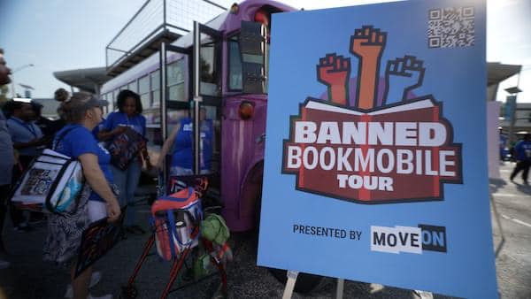 purple bookmobile with people in blue shirts waiting to enter and a sign that reads - banned bookmobile tour