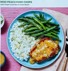 pink background with blue plate featuring rice, green beens and pork chop