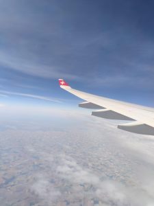 white airplane wing above the clouds with a Swiss flag on the wing tip against blue sky