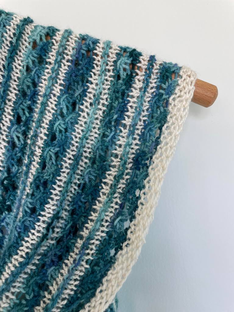 stitch detail of teal and white hand knit shawl on a wooden hanger