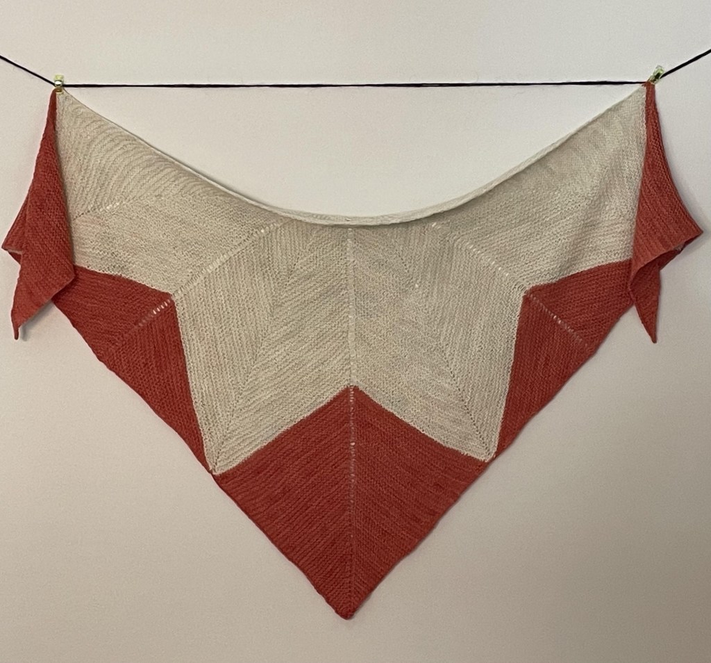 hand knit triangular shawl with a cream colored star and orange accents