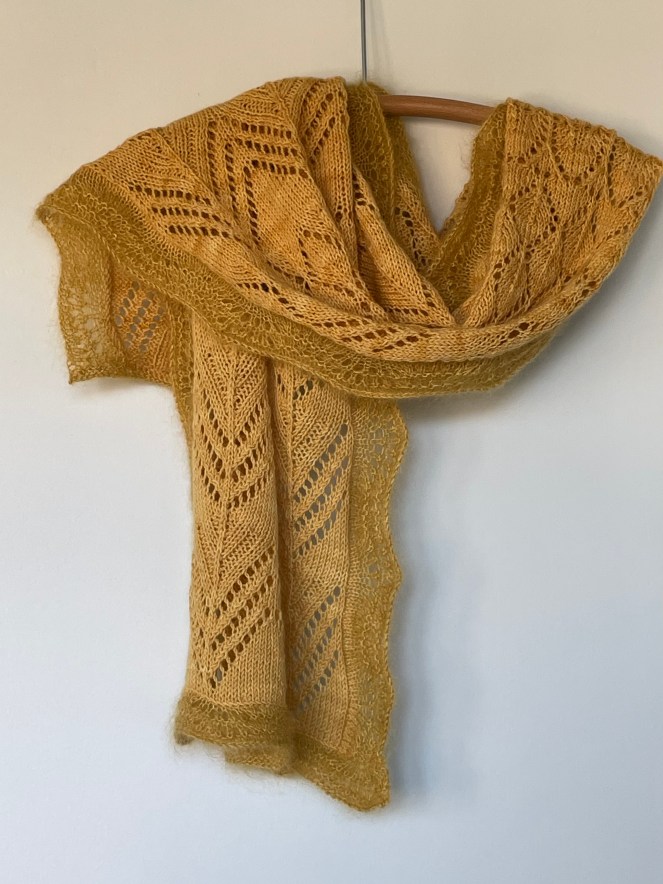 handknit lace scarf in two-toned gold yarn draped on a wooden hanger