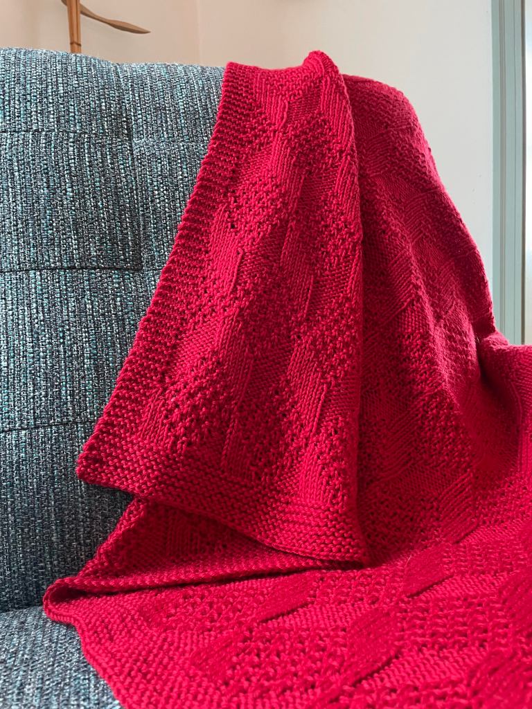 small handknit red blanket on a blue tweed chair