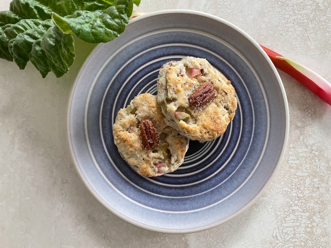 two rhubarb scones on a blue plate with one stalk of rhubarb resting along the top edge