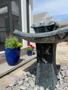 small gray, three tiered fountain in foreground with blue flower pots in the background