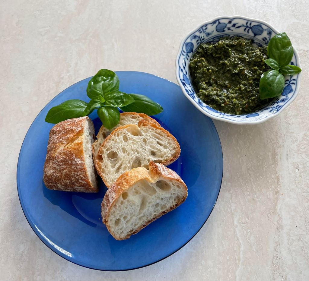 blue glass plate with three slices of french bread and a sprig of basil and a small blue and white bowl with pesto and a sprig of basil