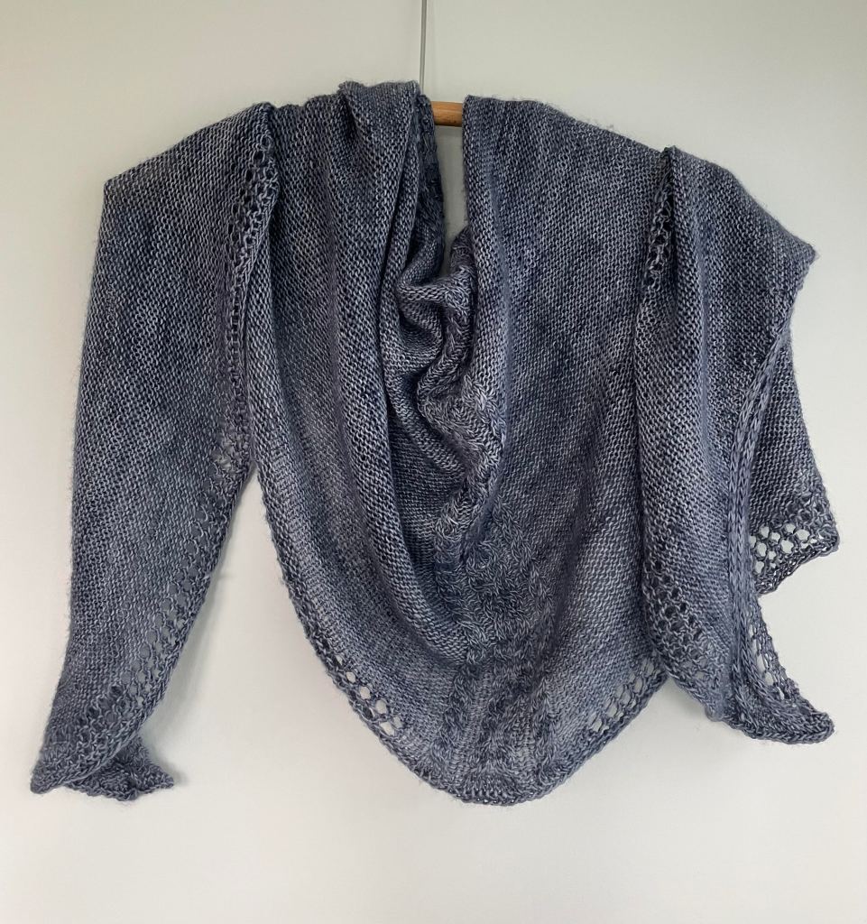blue handknit shawl draped on a wooden hanger