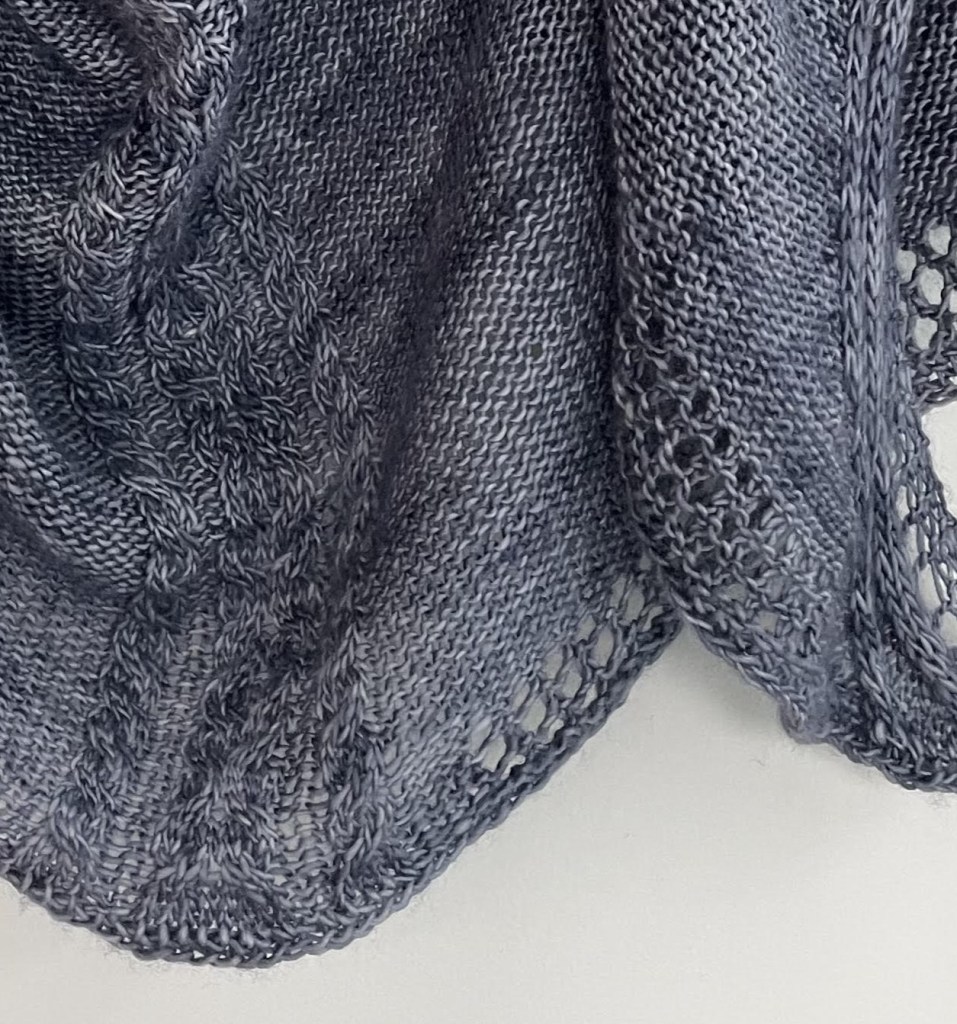 close up of knit stitches on a handknit blue shawl showing lace and cables