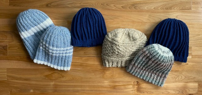 a selection of six hand knit beanies in various colors on a wood floor