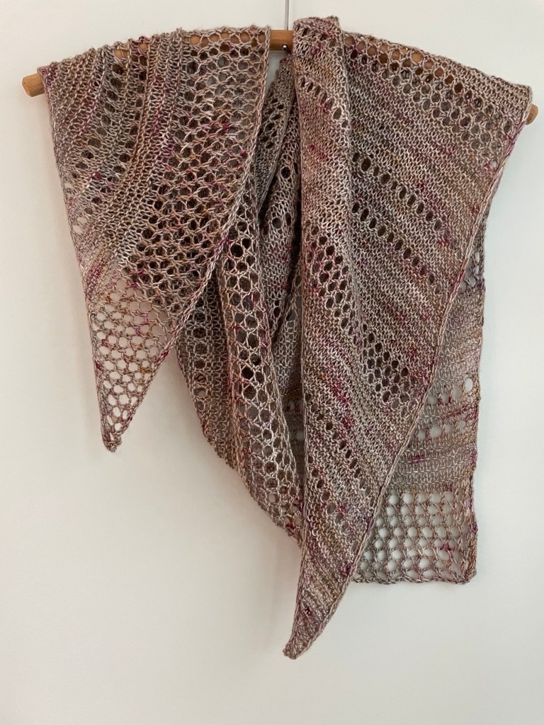 handknit shawl with rows of lace stitches in lavendar and green hues on a wooden hanger
