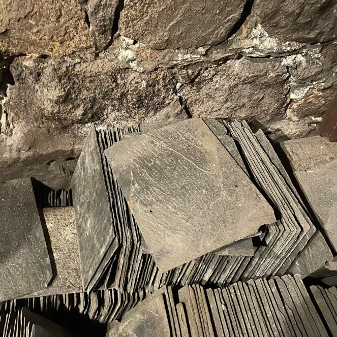 stacks of gray slate roof tiles set against old stone wall