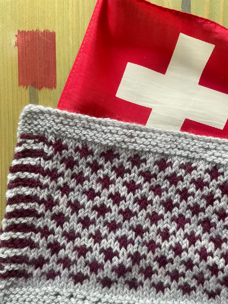 Swiss flag in the background overlaid with gray and maroon checked knitted swatch