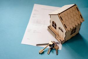 light blue background with 3-D cardboard house, housekeys, and piece of paper