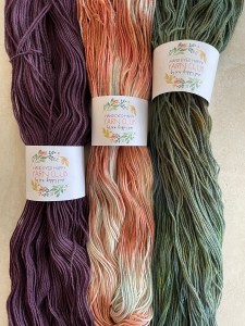 three skeins of yarn with colors (left to right) purple, varigated coral, and green