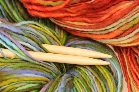 chunky varigated yarn in green and orange colors with knitting needles
