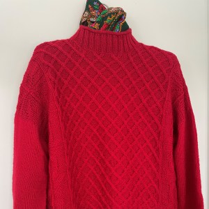 red hand knit sweater with cables on front and green scarf at the neck