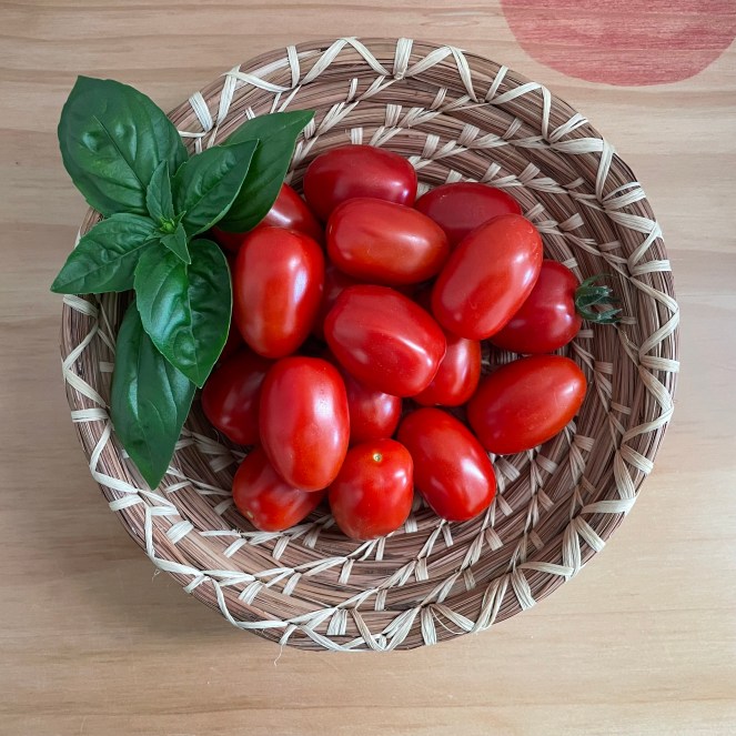 small basket filled with cherry tomatoes with a sprig of basil