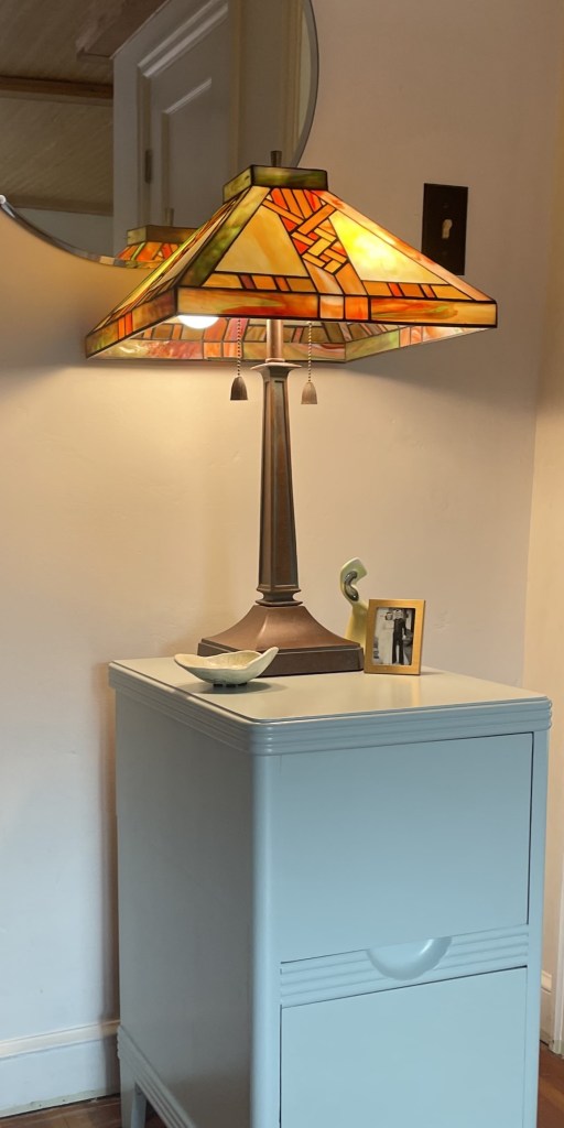two drawer nightstand with yellow lamp and round mirror