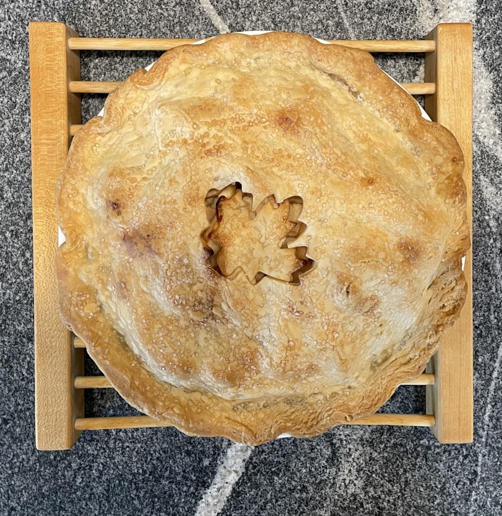 apple pie on wooden pie rest sitting on gray granite counter