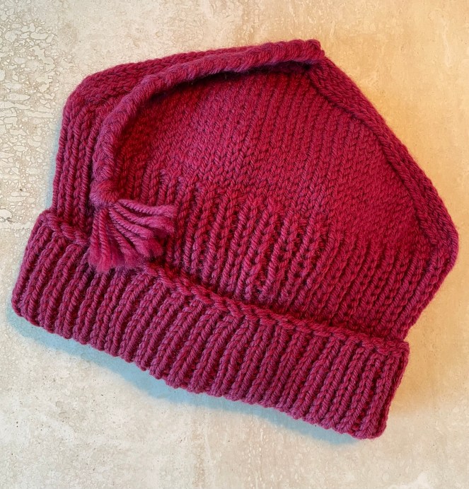 red, handknitted beanie with straight sides, pointed top and a braided tassle