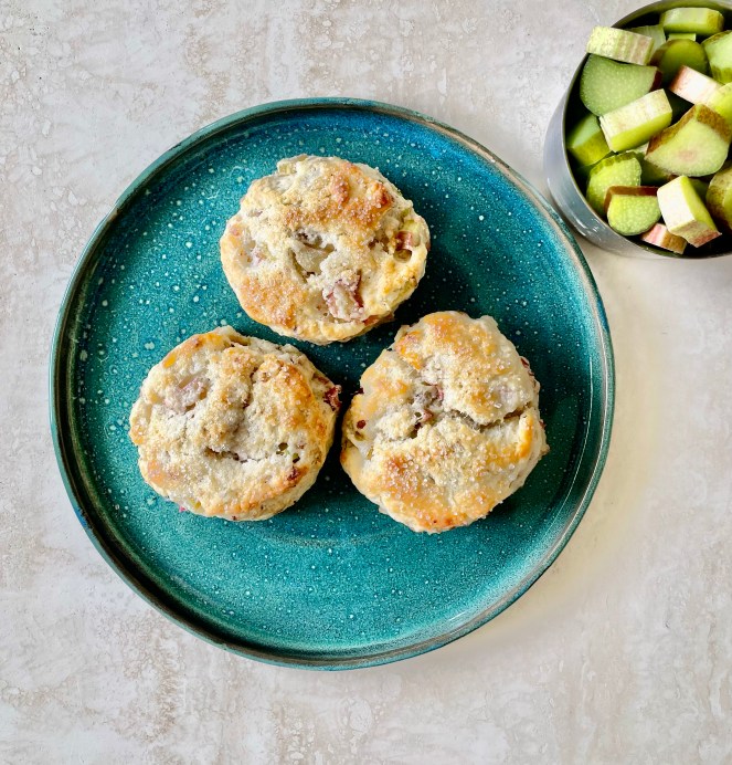 Three scones on a blue plate and a measuring cup with chopped rhubarb