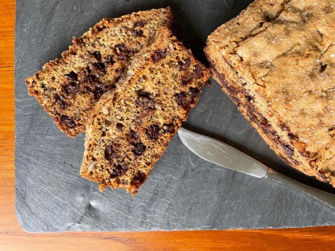 two slices of bread with chocolate chips on black slate with partial loaf of bread and a knife